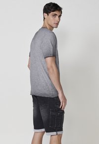 Camiseta gris de manga corta con una textura sutil y un dobladillo redondeado, combinada con pantalones cortos de mezclilla negros que tienen dobladillos enrollados y múltiples bolsillos.
