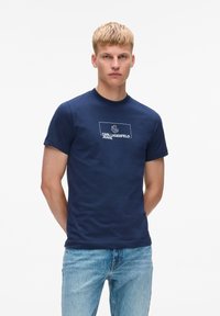 Navyblauwe katoenen T-shirt met een ronde hals en korte mouwen; voorzien van een wit logo met de tekst "KARL LAGERFELD JEANS" in een rechthoekige omranding.