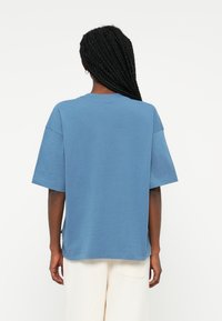 T-shirt oversized azul claro com decote redondo, mangas curtas e fendas laterais, feita de material de algodão macio. Design liso.