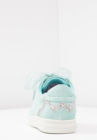 Sneaker in suede verde menta con un accento glitterato a zigzag, un fiocco in nastro trasparente e una suola in gomma bianca.