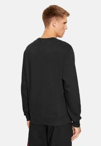 Felpa nera con scollo rotondo, maniche lunghe e polsini e orlo a costine. Materiale morbido con una texture liscia.