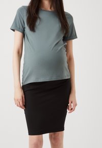 Umstandstop aus weichem, hellblaugrauem Material mit umgeschlagenen Kurzärmeln, kombiniert mit einem figurbetonten schwarzen Bleistiftrock. Glatte Textur, simples Design.