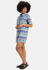 Short-sleeve button-up shirt with a multicolored geometric pattern in blue and purple. Cotton fabric, relaxed fit, knee-length shorts.