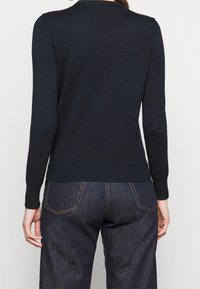 Navy blue knitted sweater with long sleeves, ribbed hem, and textured neckline detail. Paired with dark denim jeans.