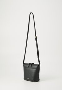 Svart lær crossbody-veske med justerbar stropp, magnetisk lukking og to toppsløyfer. Har en gulllogo-detalj på forsiden.