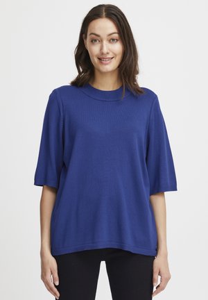 Top in maglia blu con maniche corte e collo rotondo, indossato da un modello su uno sfondo semplice. Tessuto liscio con vestibilità comoda.
