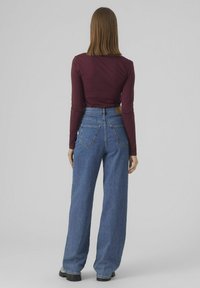 Un haut bordeaux à manches longues associé à un jean bleu large taille haute. Le jean comporte cinq poches et une finition en denim texturé.