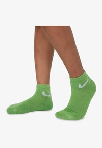Zöld boka zoknik textúrált kötött anyagból, a külső oldalon fehér Nike logóval.