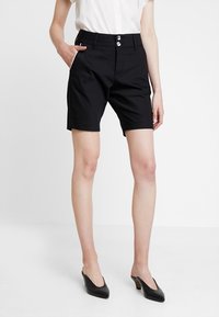 Czarne bawełniane szorty o dopasowanym kroju, z dwiema przednimi kieszeniami i srebrnymi guzikami. Posiadają gładką teksturę i długość do połowy uda.