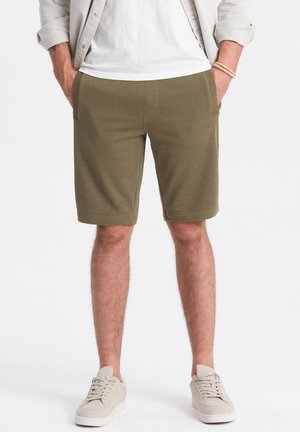 Olivgrüne Shorts aus Baumwollmischung mit zwei Vordertaschen und geradem Schnitt, kombiniert mit beigen Sneakers.