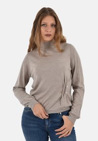 Maglione a dolcevita beige chiaro, texture morbida, maniche lunghe, con bottoni decorativi sui lati, abbinato a jeans blu.