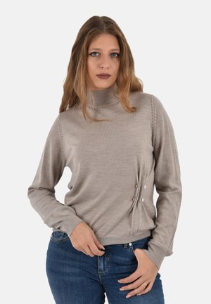 Maglione a dolcevita beige chiaro, texture morbida, maniche lunghe, con bottoni decorativi sui lati, abbinato a jeans blu.