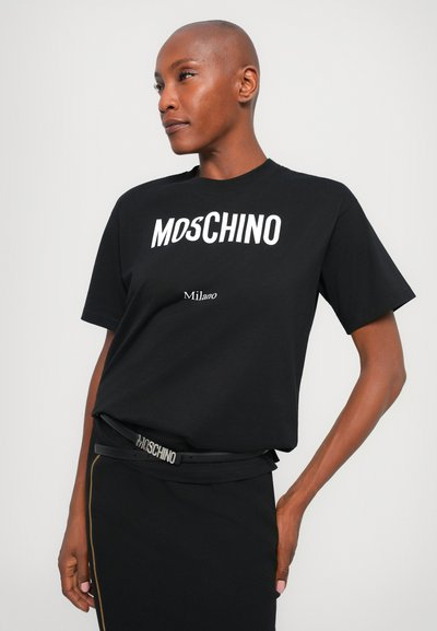 T-shirt en coton noir avec un logo "MOSCHINO" en blanc très visible et un texte "Milano" en plus petit, associé à une ceinture noire affichant le même nom de marque.