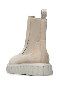Beige kotníkové boty vyrobené z jemné kůže s elastickými bočními panely, robustní bílou podrážkou a poutkem na zadní straně pro snadné obouvání.
