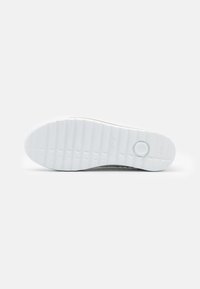 White sneaker sole with textured grooves and circular emblem. Features a smooth surface and slight curvature towards the heel.