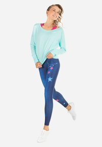 Svetlomodrá blúzka s dlhým rukávom skombinovaná s tmavomodrými legínami s mnohobarevnými hviezdami. Biely športový obuv dotvára outfit.