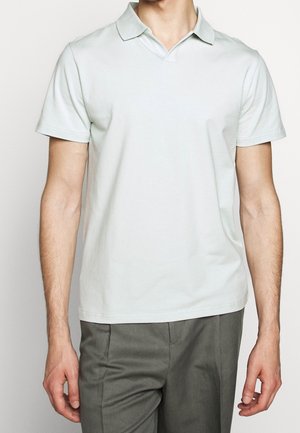 Light green polo shirt made of cotton, featuring a classic collar, short sleeves, and a relaxed fit, paired with gray trousers.