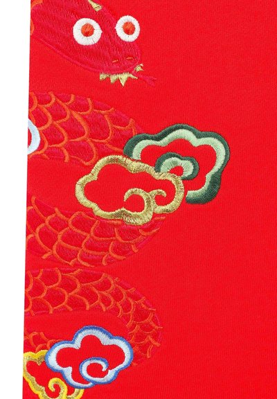Un tissu rouge présente une broderie complexe en or et multicolore illustrant un dragon et des nuages stylisés, mettant en valeur des écailles détaillées et des accents.