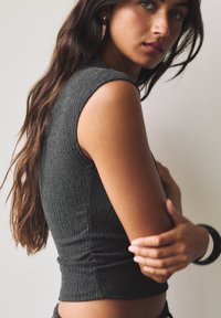 Haut gris sans manches en maille côtelée avec une silhouette ajustée, présentant un ruché à la taille et une finition lisse et texturée.