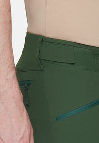 Groene sportbroek met een gladde textuur, voorzien van een elastische tailleband, zijzak met rits en een vlakke voorpaneelontwerp.