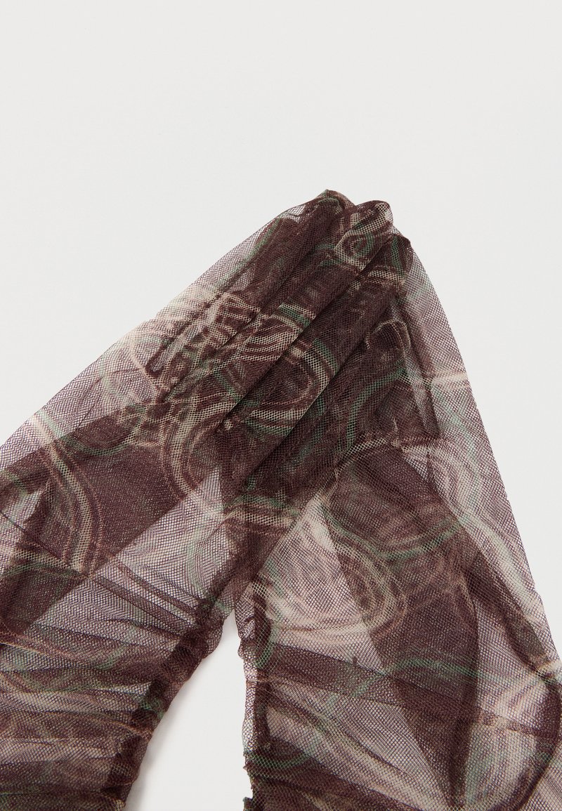 Tissu en maille brune transparente à motifs, plié sur un fond blanc, montrant une texture fine et translucide avec des tourbillons abstraits.