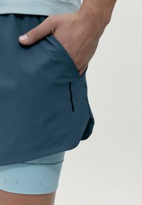 Shorts gjorda av ljusblå och mörkblå material, med en sidoficka och en slank design med minimal sömnad och accenter.