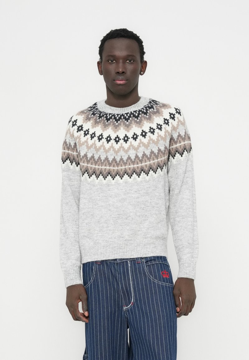 Γκρι πουλόβερ με μοτίβο Fair Isle σε καφέ και μαύρο, στρογγυλή λαιμόκοψη και ριμπ μανσέτες. Συνδυασμένο με μπλε τζιν με λεπτές ρίγες.