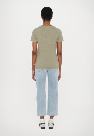Olivgrön t-shirt med kort ärm, bomullsblandning, figurnära passform, bärs med ljusblå raka jeans och vita strumpor, sedd bakifrån.