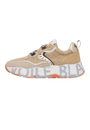 Zapatilla beige y canela con textura tejida, detalles en ante, suela blanca con grandes letras grises parciales y detalles en la suela externa de color naranja.