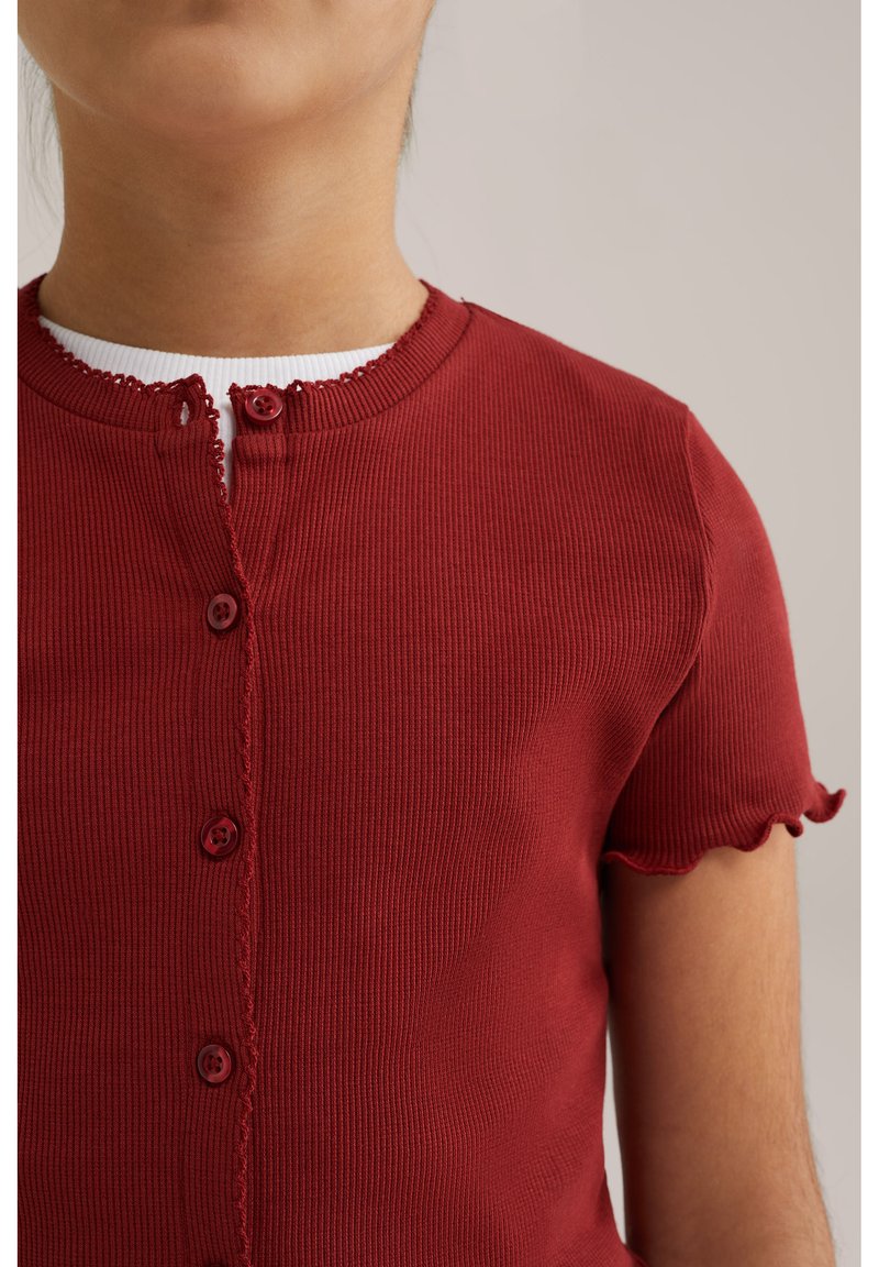 Camicetta rossa a righe con maniche corte, colletto rotondo, bordi decorativi a scallop e quattro bottoni abbinati sul davanti.