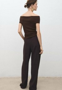 Top in maglia marrone scollato con spalle scoperte abbinato a pantaloni larghi marrone scuro. Il modello è mostrato di spalle, evidenziando la vestibilità e la silhouette.