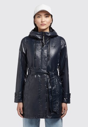 Capa de lluvia impermeable azul marino con un acabado brillante, capucha con cordón, cintura ceñida con cinturón y puños abotonados. Presenta un sutil branding en la parte frontal.