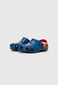 Blue clog-style shoes featuring a textured design, red accents, and a prominent yellow "S" logo. Made from lightweight material with ventilation holes.