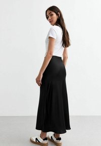 Zwarte, vloeiende maxi-jurk gemaakt van zacht materiaal, gecombineerd met een aansluitend wit T-shirt en witte sneakers met zwarte accenten en een gestructureerde zool.