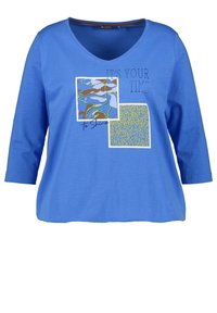 T-shirt blu con maniche a tre quarti e scollatura a V, caratterizzato da stampe grafiche in colori contrastanti e testo che dice: "È il tuo momento di brillare."