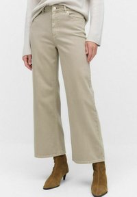 Beiga vida jeans gjorda av kraftigt tyg, med hög midja, framfickor och subtila sömnadsdetaljer. Kombineras med bruna ankelstövlar.