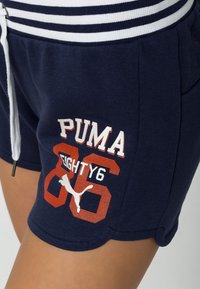 Marina bomullsshorts med randig midja. Har grafik med "PUMA" och "EIGHTY6" i vitt och orange. Inkluderar en dragkedjedetalj.