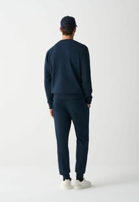 Mornarji modra majica in dolge hlače iz mehkega materiala, z ribastimi manšetami in minimalističnim dizajnom, v kombinaciji z belimi supergami.