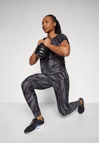 Treningsantrekk med svarte og grå tigerstripede leggings og matchende t-skjorte. Svart kettlebell, svarte sportsko med grå detaljer.