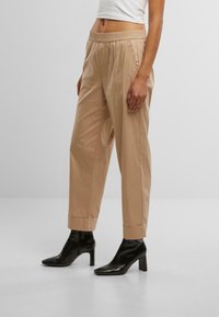 Pantaloni di cotone beige con vita elastica, gamba affusolata e orli arrotolati, abbinati a stivaletti neri con tacco.