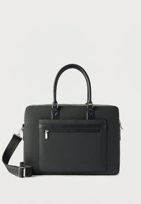 Mallette rectangulaire noire avec poignées supérieures, poche zippée à l'avant et bandoulière détachable avec le logo Lacoste.