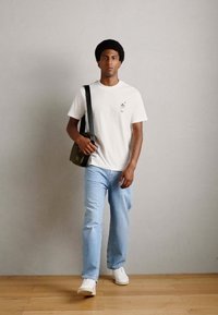 Witte katoenen t-shirt met een kleine graphic op de borst, gecombineerd met lichtblauwe rechte jeans en witte sneakers. Verstelbare schoudertas.