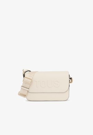 Bolso cruzado de imitación cuero en color crema con el logo "TOUS" en relieve, correa ajustable y herrajes en tono dorado. Textura suave, forma rectangular.