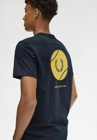 Camiseta de algodón azul marino con un gran gráfico de pelota de tenis amarilla y acentos de laurel en la parte posterior. Cuello redondo, mangas cortas, corte relajado.