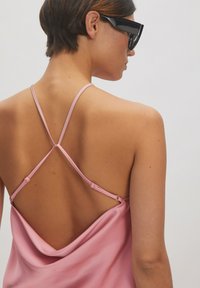 Roze zijden camisole met een gedrapeerde achterkant en dunne, verstelbare bandjes, met een open rugontwerp. Model draagt zwarte zonnenbril.