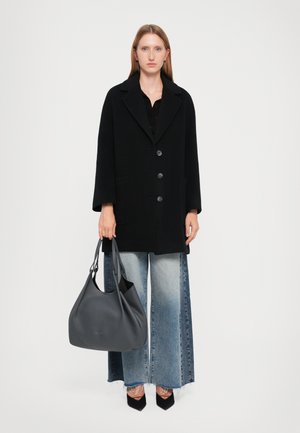 Cappotto in tessuto misto lana nera con grandi bottoni e due tasche, abbinato a jeans in denim a gamba larga. Una borsa in pelle grigia completa l'outfit.