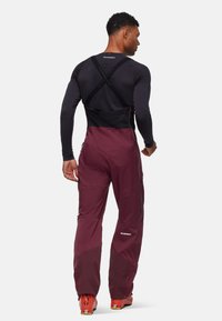 Maroon ski broek met een zwarte tailleband en ritsen, voorzien van een slim fit en versterkte onderbenen. Draagt over een zwarte lange mouwen top.