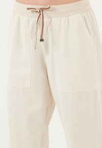 Beige, lichtgewicht broeken met een elastische tailleband en trekkoord. Voorzien van twee zijzakken en subtiele stikdetails.