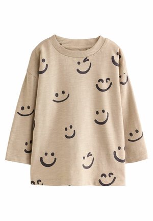 Beige skjorte med lange ærmer med flere sorte smileys, herunder blinkende og lukkede øjne, trykt over hele stoffet.