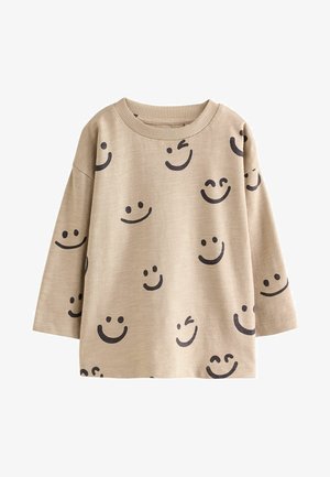 Beige skjorte med lange ærmer med flere sorte smileys, herunder blinkende og lukkede øjne, trykt over hele stoffet.